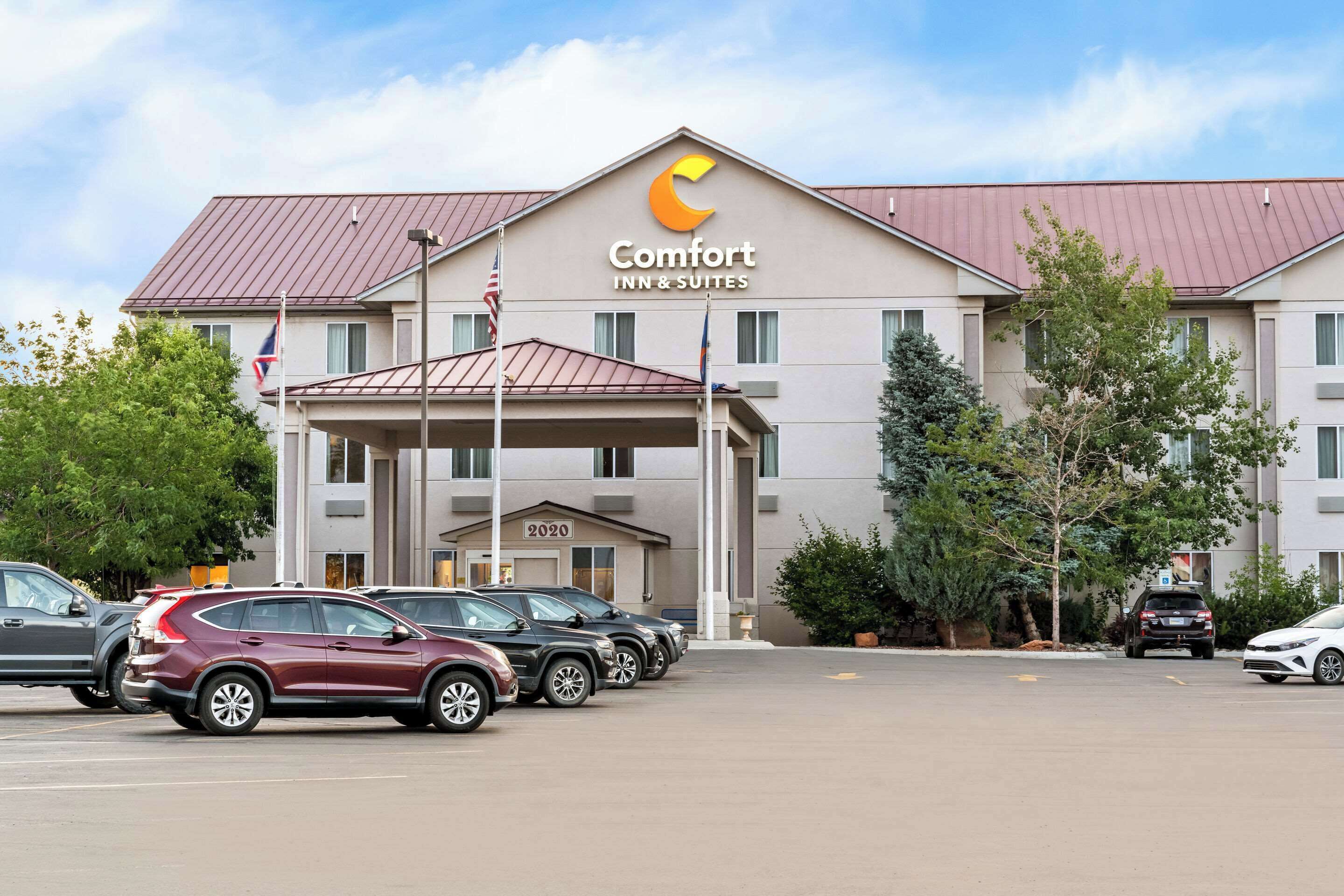 A Comfort Inn & Suites hotel with a modern design, featuring a prominent logo, a covered entrance, and a parking lot with several cars.