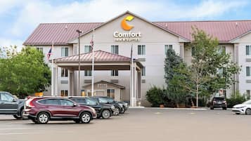 A Comfort Inn & Suites hotel with a modern design, featuring a prominent logo, a covered entrance, and a parking lot with several cars.