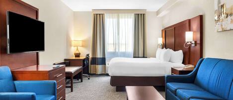 A hotel room with a bed, a desk, a TV, a blue sofa, and a lamp.