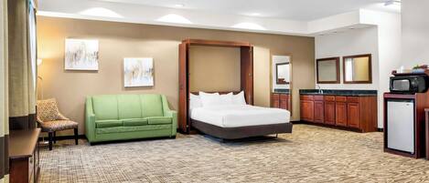 A hotel room with a bed, a green sofa, a small kitchenette, and artwork on the walls.
