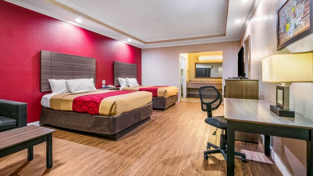 Quarto de hotel com duas camas, uma escrivaninha, uma cadeira e uma mesinha.
