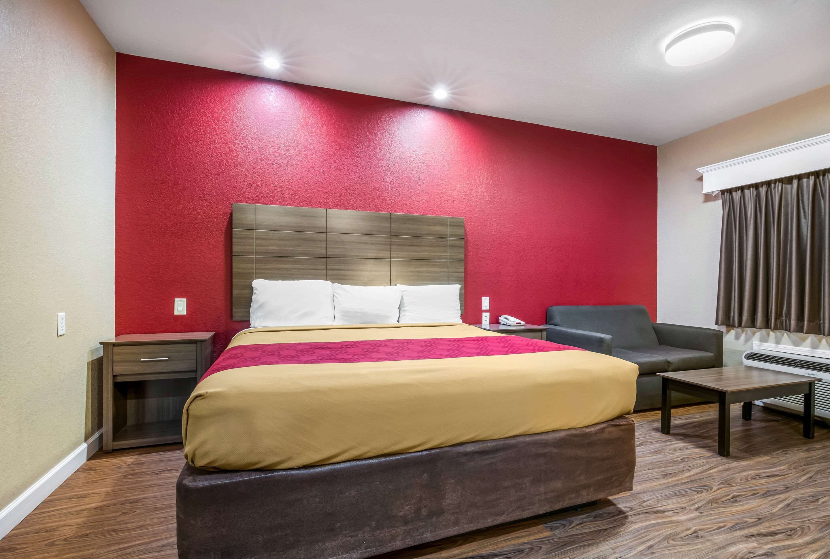 Een hotelkamer met een groot bed, een nachtkastje, een stoel, een bureau en een raam met gordijnen.