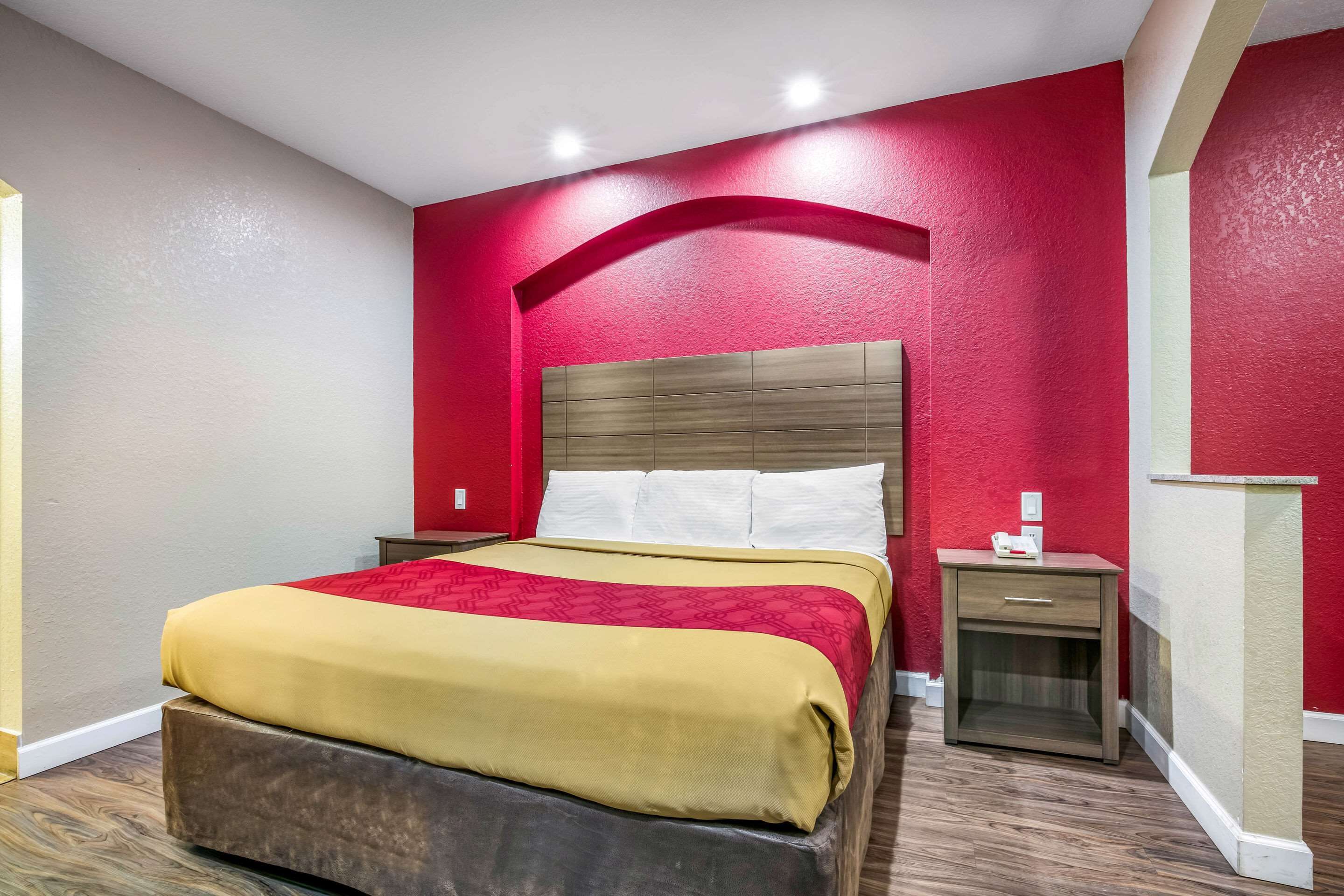 A hotel room with a bed, bedside table, and a red accent wall.