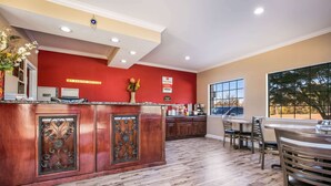 Um saguão de hotel com uma receção de madeira, parede vermelha e uma grande janela com vista para árvores.