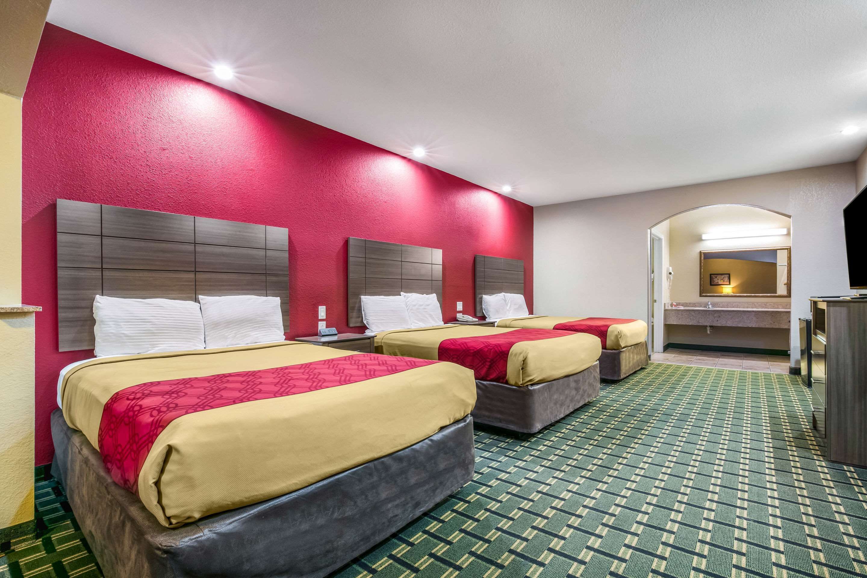 A hotel room with two beds, a green patterned carpet, and a red accent wall.