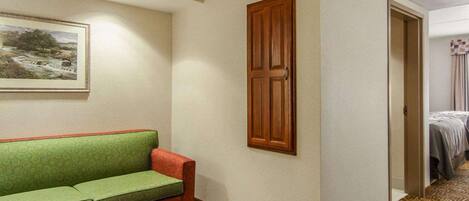 A hotel room with a green sofa, a wooden table, a painting on the wall, and a patterned carpet.