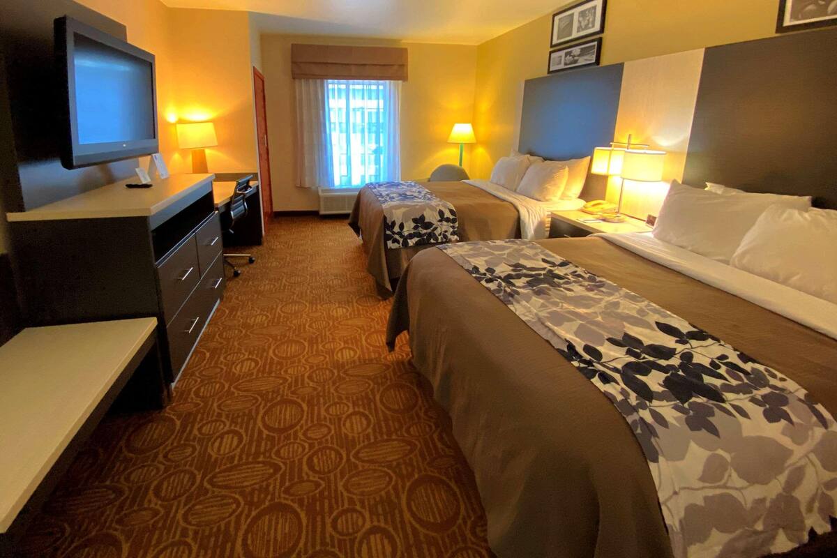 A hotel room with two beds, a desk, a television, and lamps.