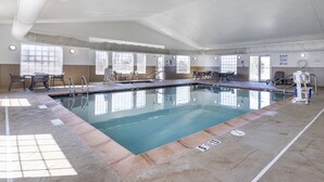 An indoor swimming pool with clear water, tiled flooring, and multiple seating areas around the pool.