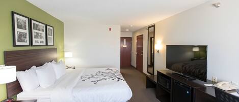 Habitación de hotel con cama, mesita de noche, lámpara, televisión y un refrigerador pequeño.