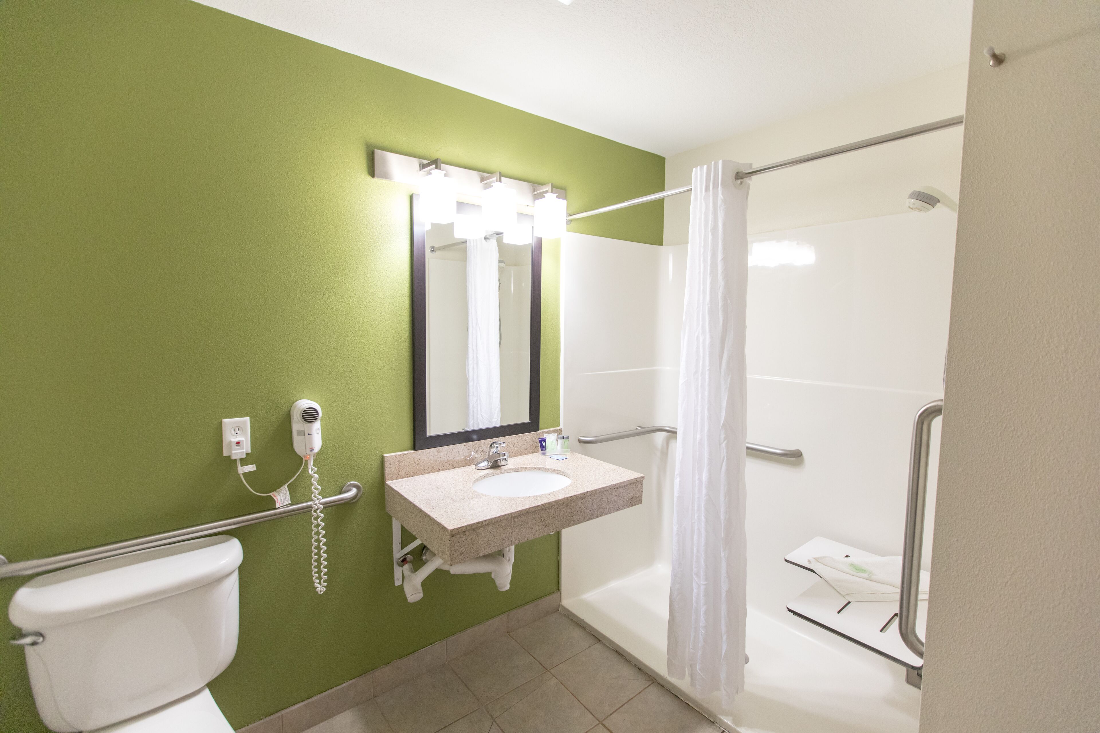 A bathroom with a green wall, a white sink, a mirror, a toilet, and a shower with a glass door.