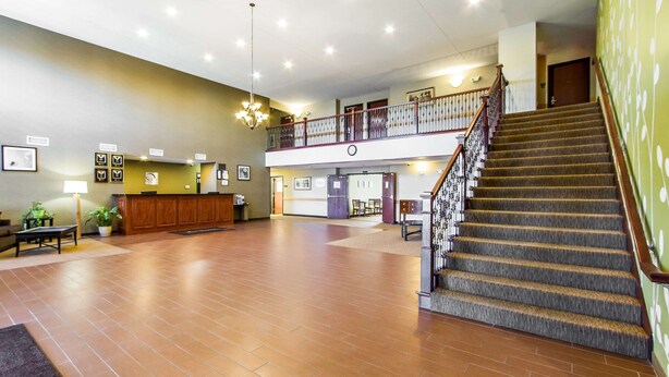 A spacious lobby with a wooden reception desk, a staircase, and a second-floor balcony.