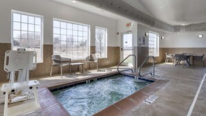 An indoor pool area with a hot tub, seating, and a view of the outdoors.