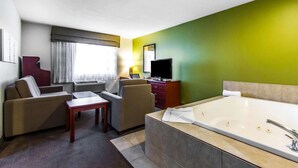 A hotel room with a sofa, armchair, small table, TV, and a large bathtub.