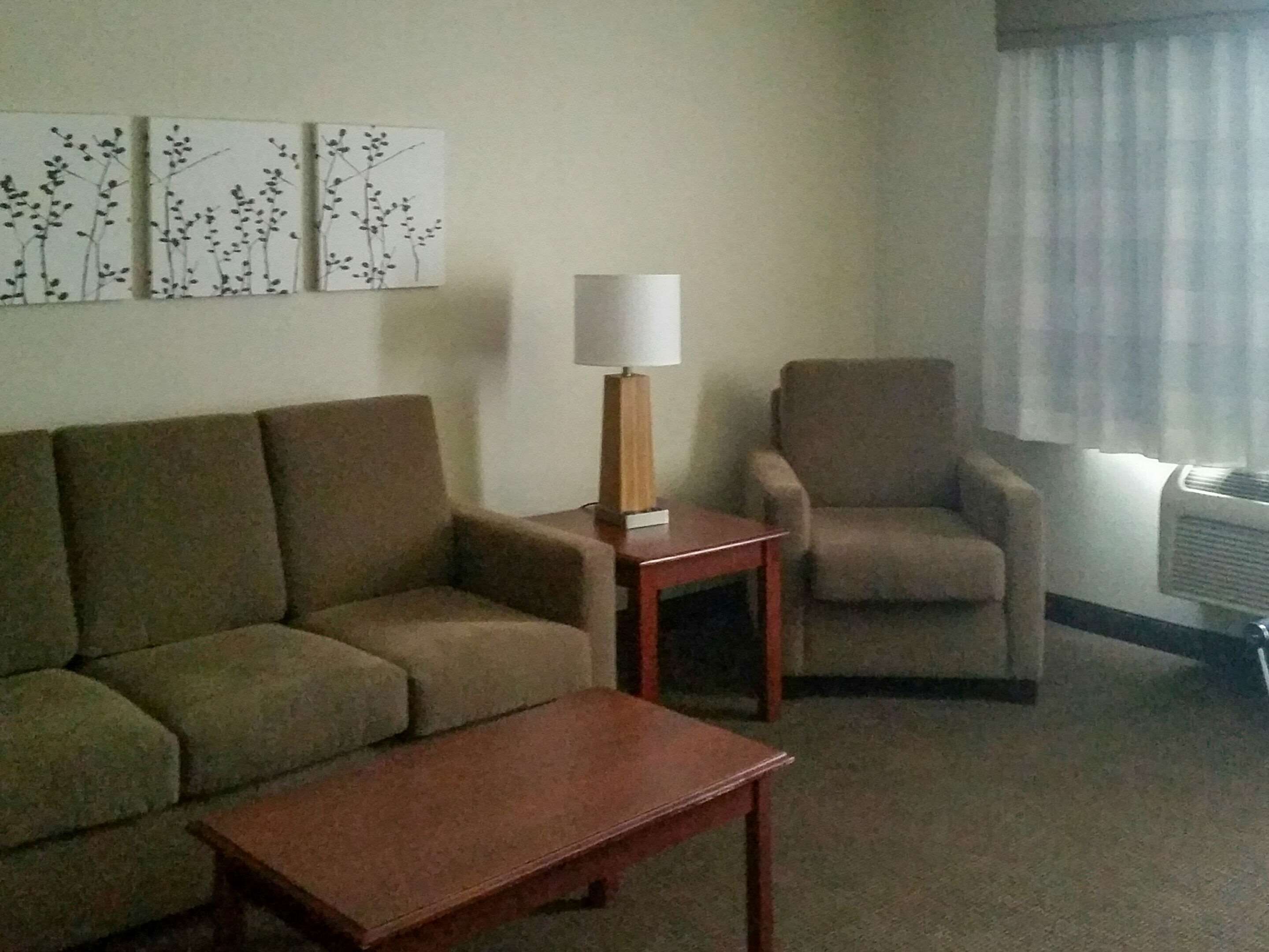 A living room with a sofa, armchair, and a small table. There are wall art pieces above the sofa.