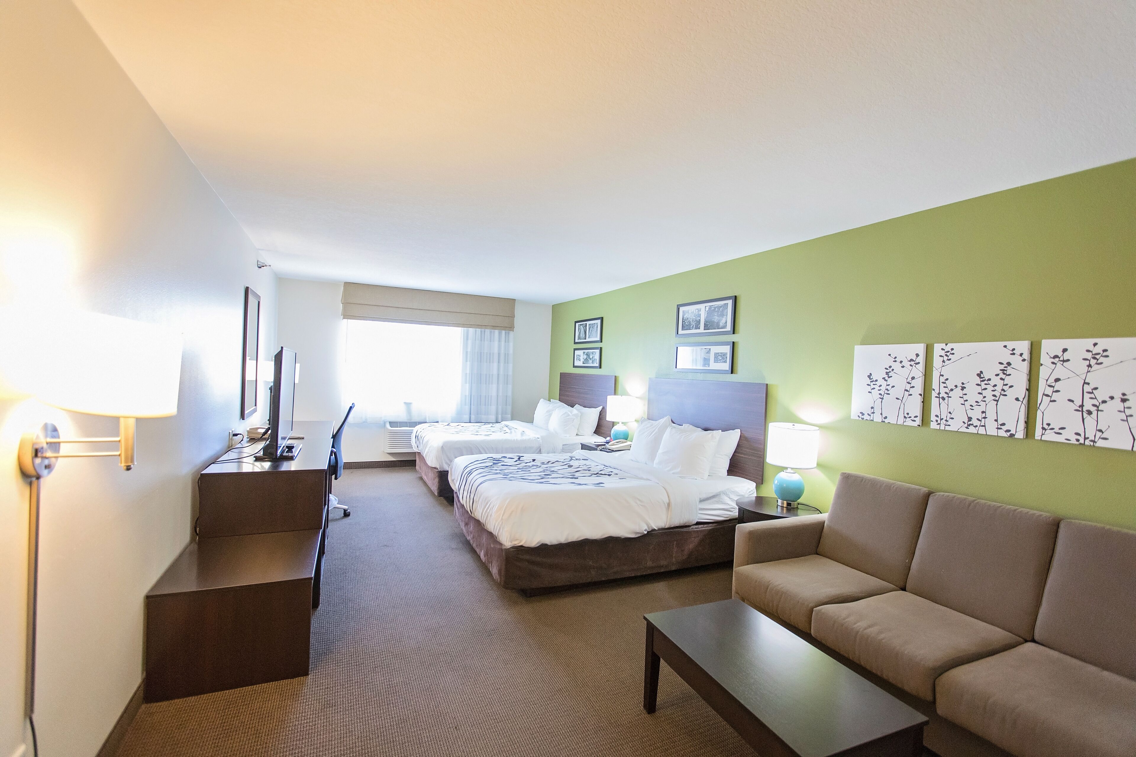 Hotellihuone, jossa on sänky, kaksi yöpöytää, sohva, työpöytä ja lamppu.