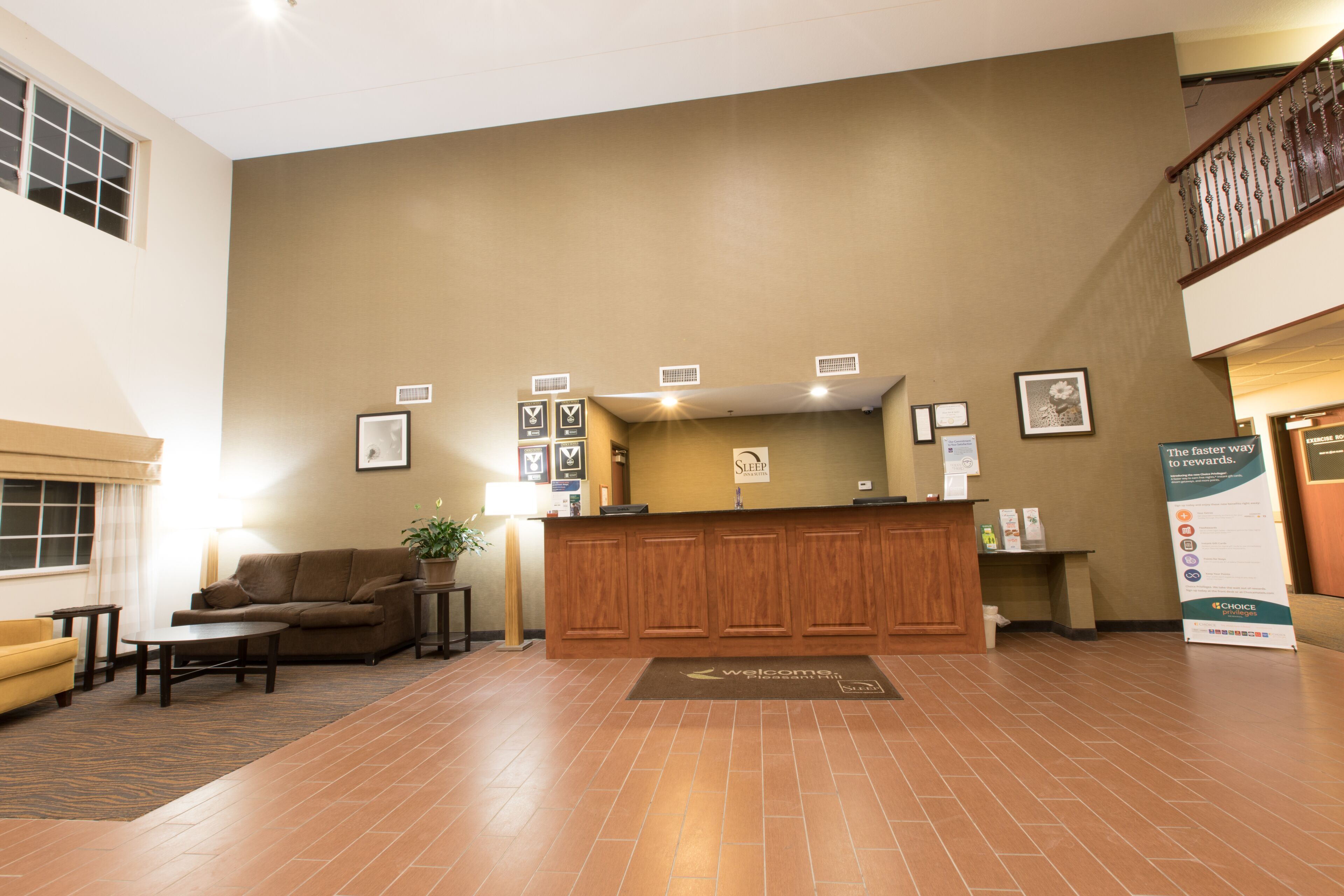 A reception area with a wooden desk, a sofa, and a coffee table. There are framed pictures on the wall and a sign that says "Welcome".