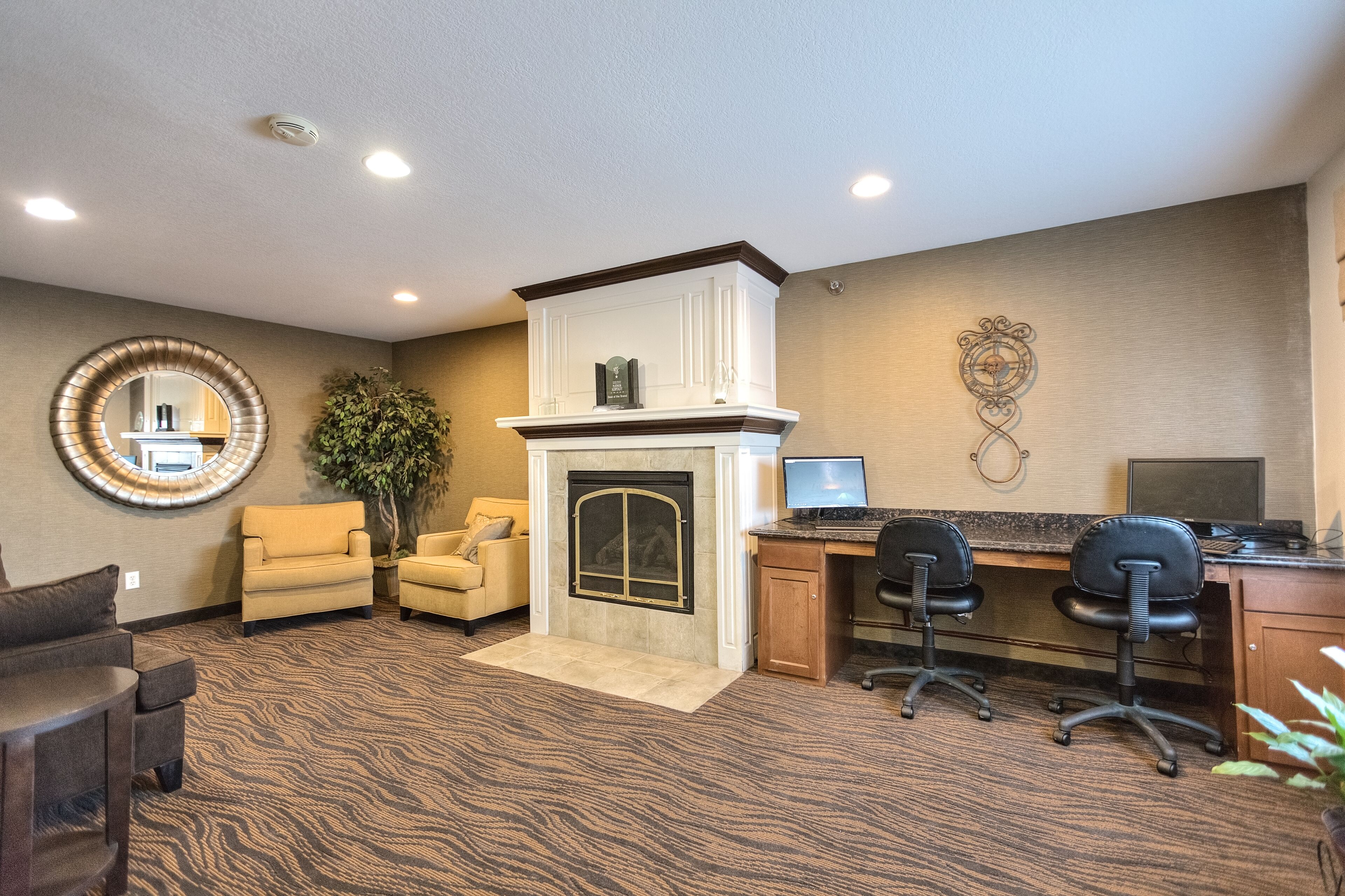 A room with a fireplace, a desk with two chairs, a round mirror, and a potted plant.