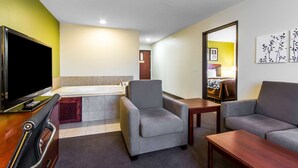 A hotel room with a flat-screen TV, a sofa, a chair, a small table, and a bathroom with a bathtub.