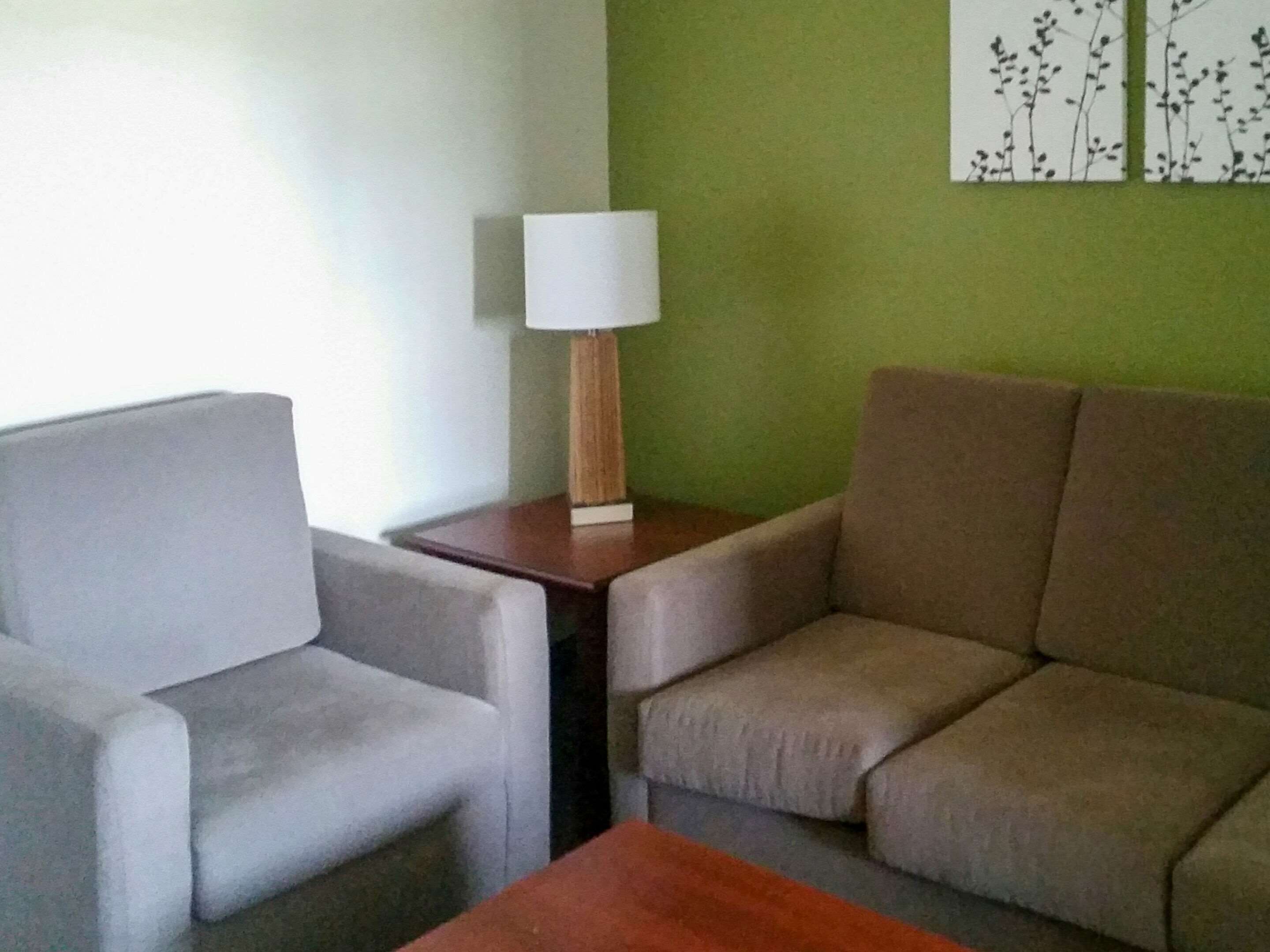 A living room with a grey sofa, a brown armchair, and a wooden side table with a lamp.