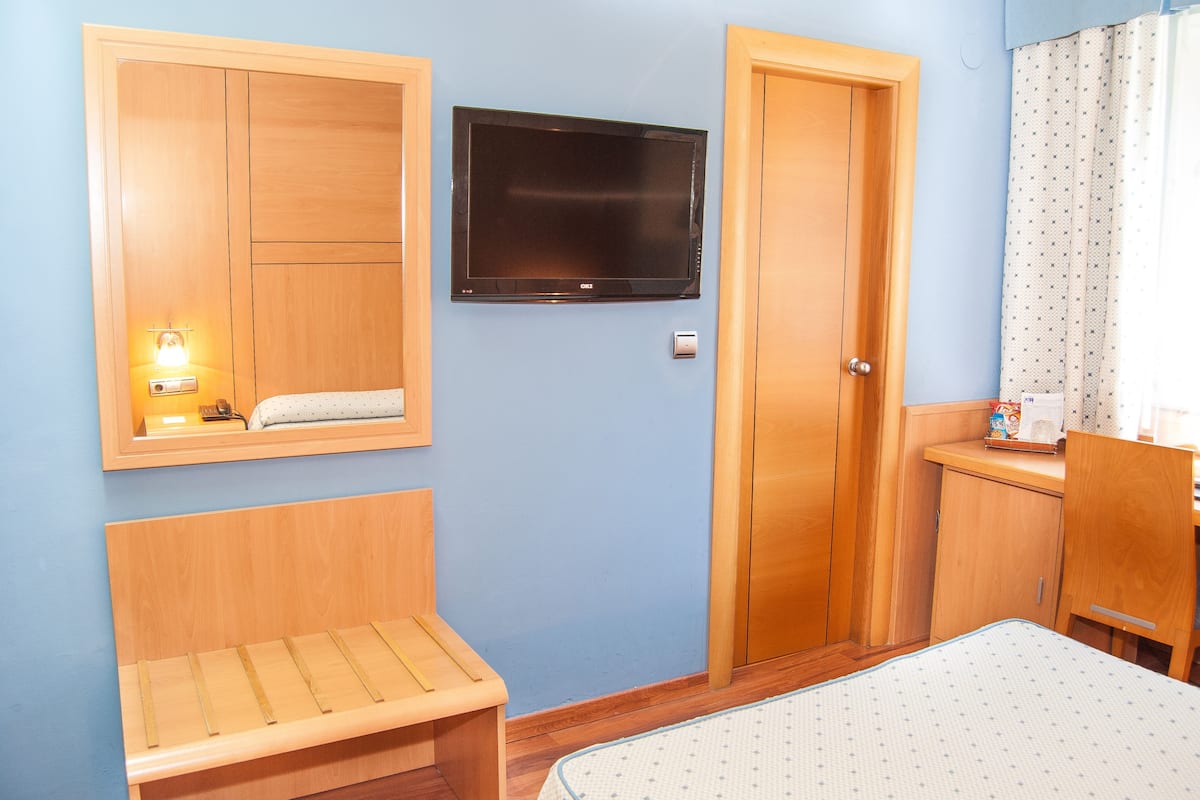 A room with a wooden bench, a television mounted on the wall, and a door with a small cabinet beside it.