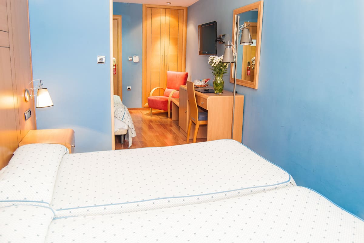 A hotel room with a bed, a desk, a chair, and a mirror.