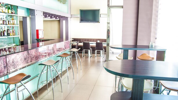 Een moderne bar met een marmeren aanrecht, barkrukken en een televisie aan de muur.