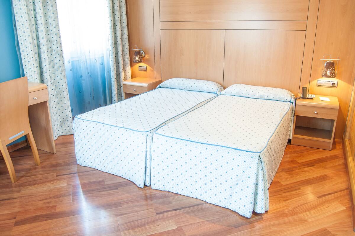 A double bed with a polka dot bedspread, a bedside table with a lamp, and a wooden headboard.
