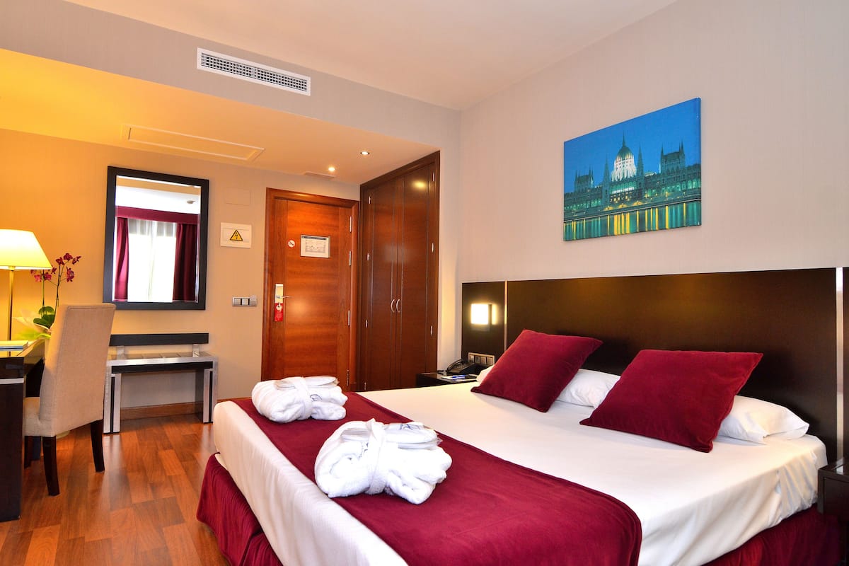 Una habitación de hotel con una cama, un escritorio, una silla, una lámpara y un cuadro en la pared.