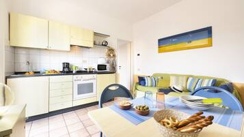 A compact kitchen with a dining area, a sofa, and a painting on the wall.