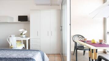 Un dormitorio con cama, escritorio, silla y mesa con tazas y tetera.