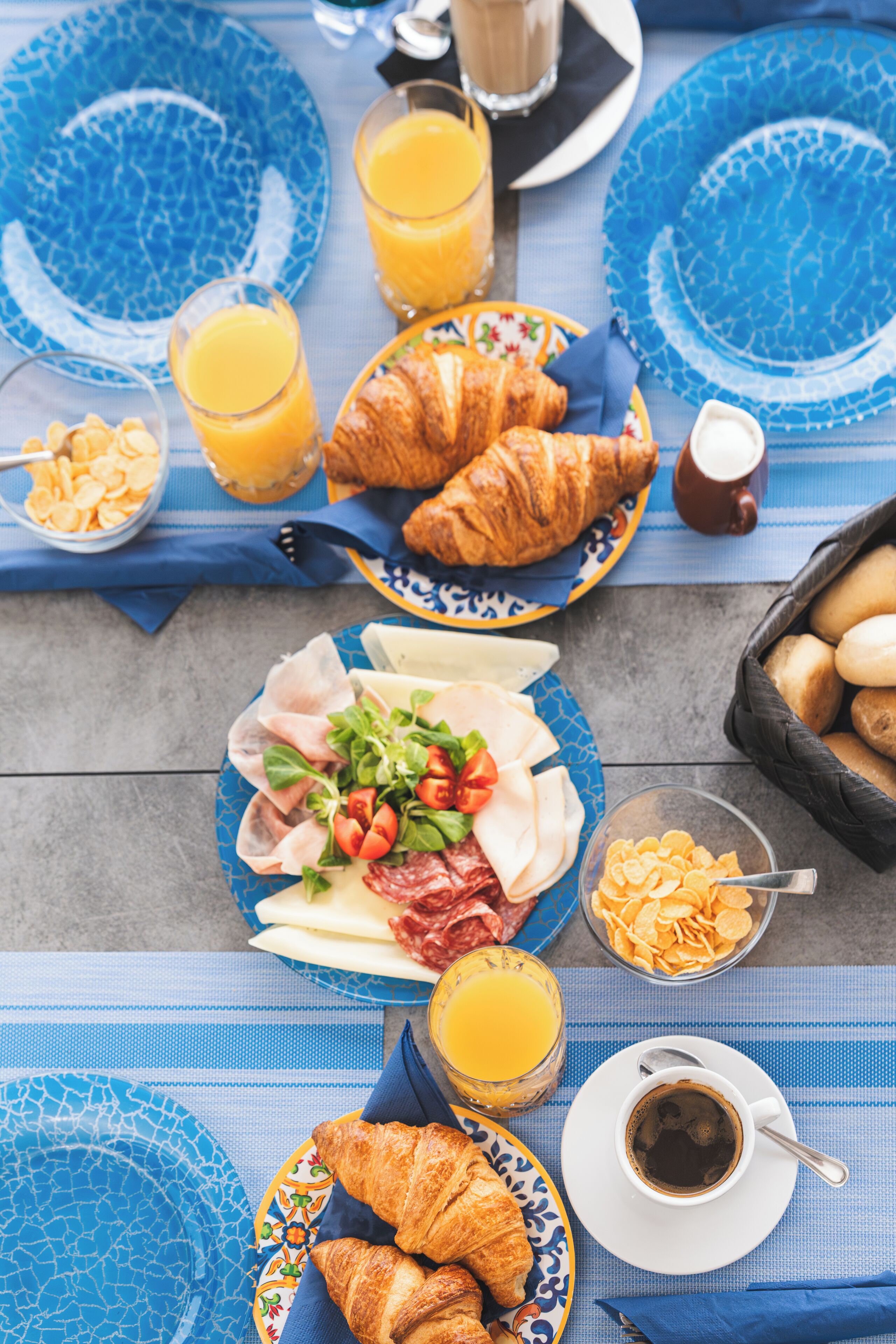 A breakfast table with croissants, cheese, tomatoes, and a croissant plate.