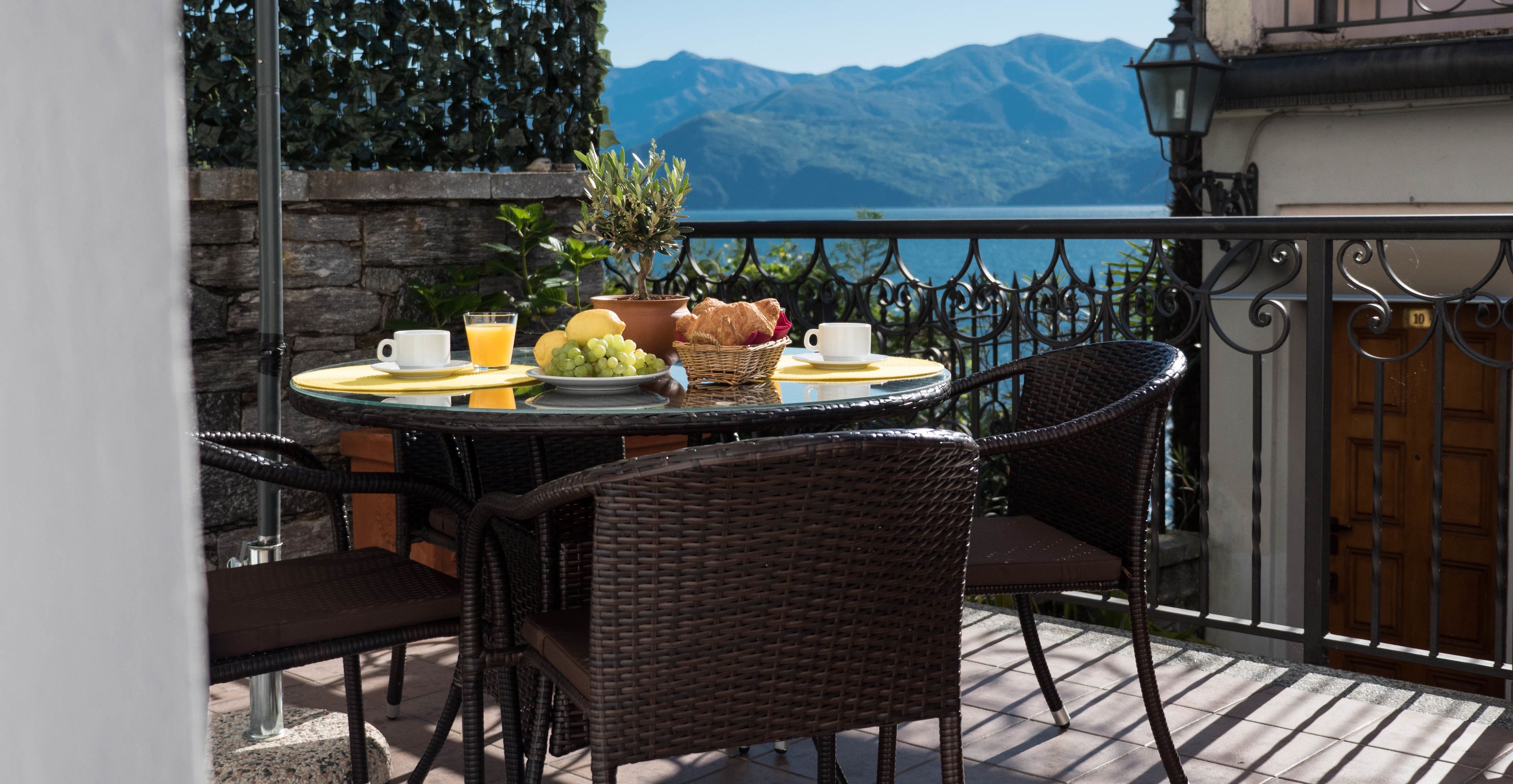 A round table with wicker chairs on a balcony overlooking a lake and mountains.