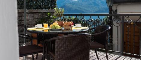A round table with wicker chairs on a balcony overlooking a lake and mountains.