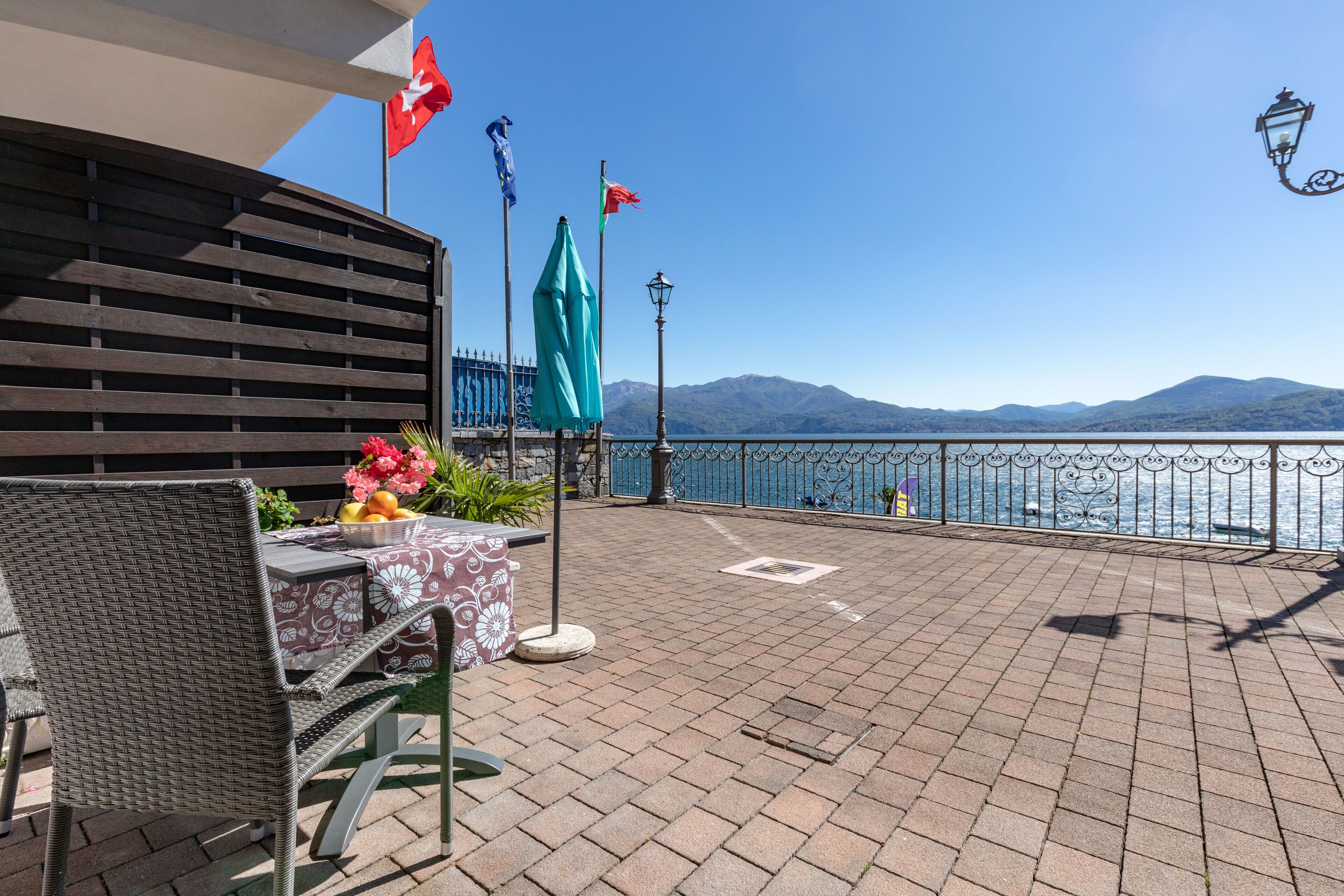 A terrace with a table and chairs, a view of the sea, and flags.