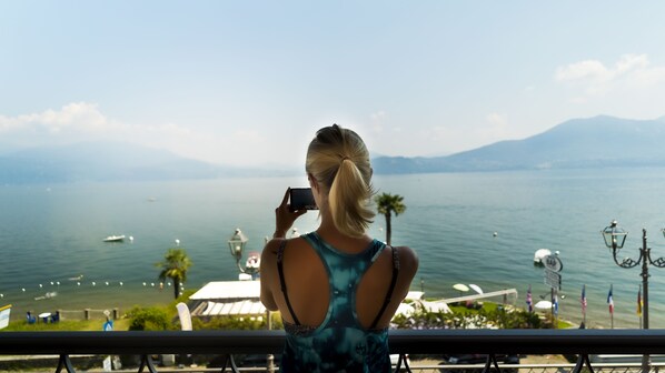 A person taking a photo of a lake with boats, a mountain in the background, and a view of the sea from a balcony. - Residence Casa e Vela (Oggebbio)
