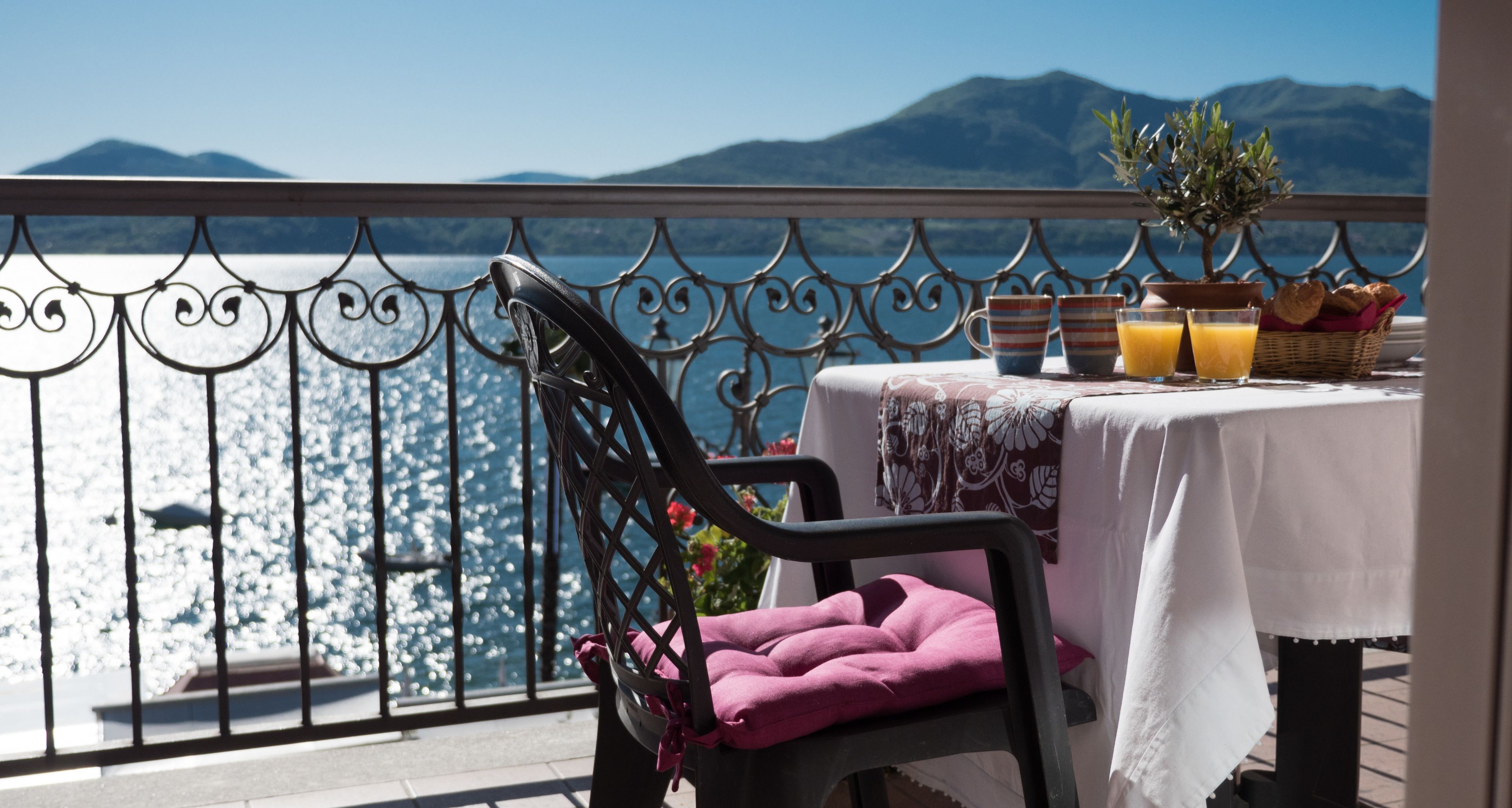 A balcony with a table set for breakfast, overlooking a body of water and mountains.