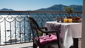 A balcony with a table set for breakfast, overlooking a body of water and mountains.