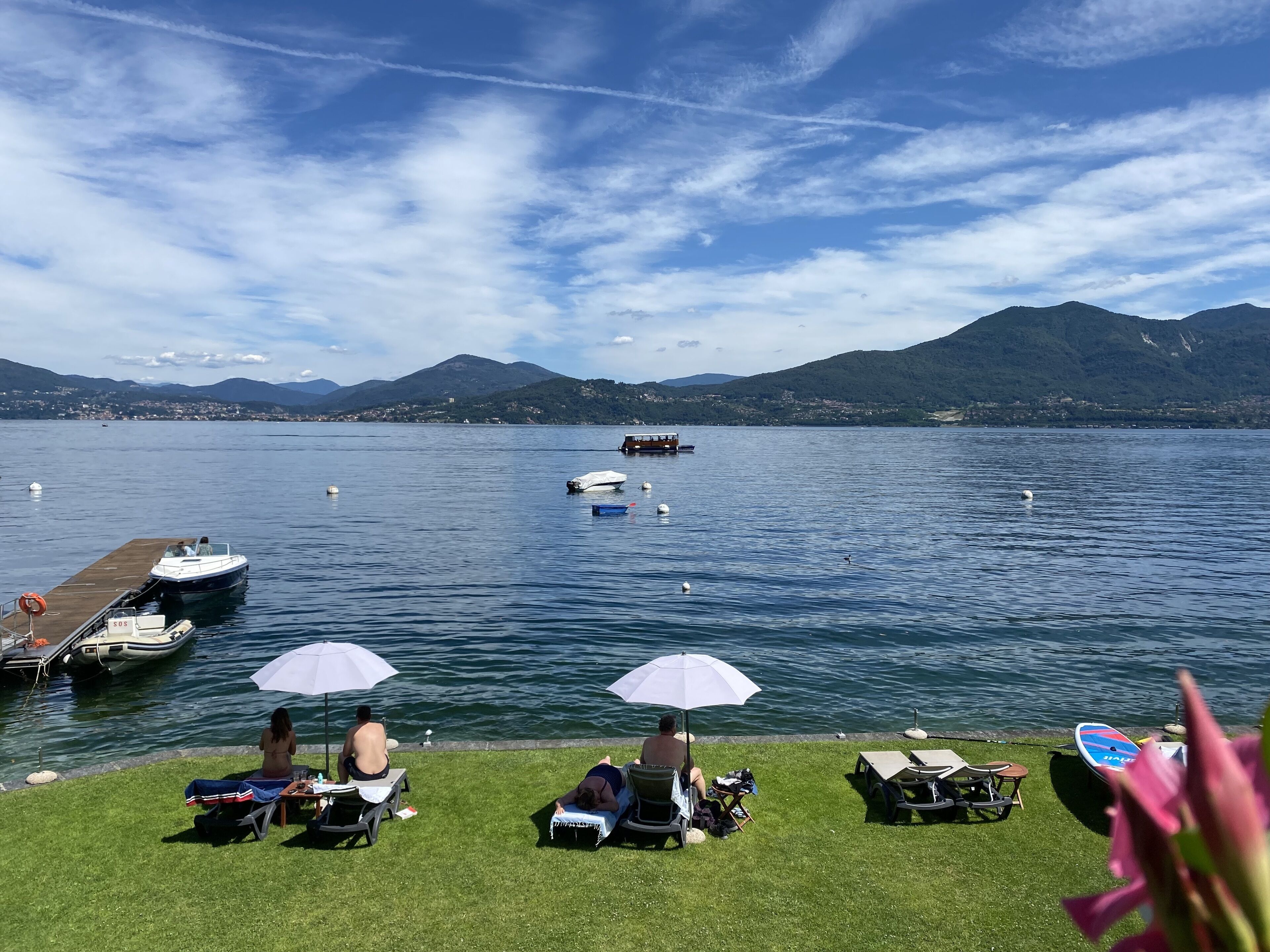 Uitzicht op een meer met boten, een steiger en mensen die ontspannen onder parasols.