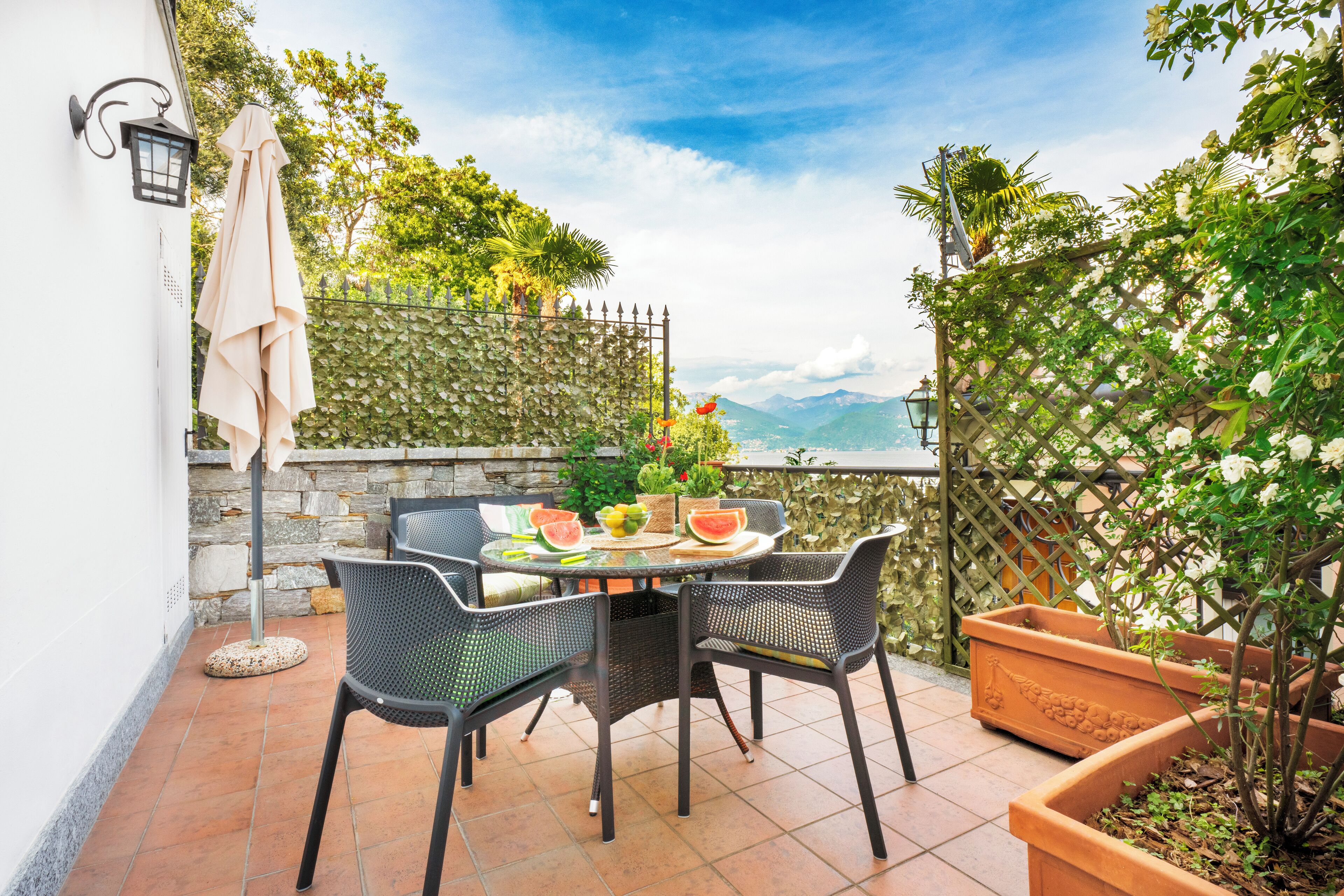 An outdoor patio with a round table and chairs, surrounded by potted plants and a stone wall.