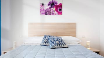 Un dormitorio con una cama, cabecera de madera, dos almohadas, una lámpara de pared y una obra de arte floral.
