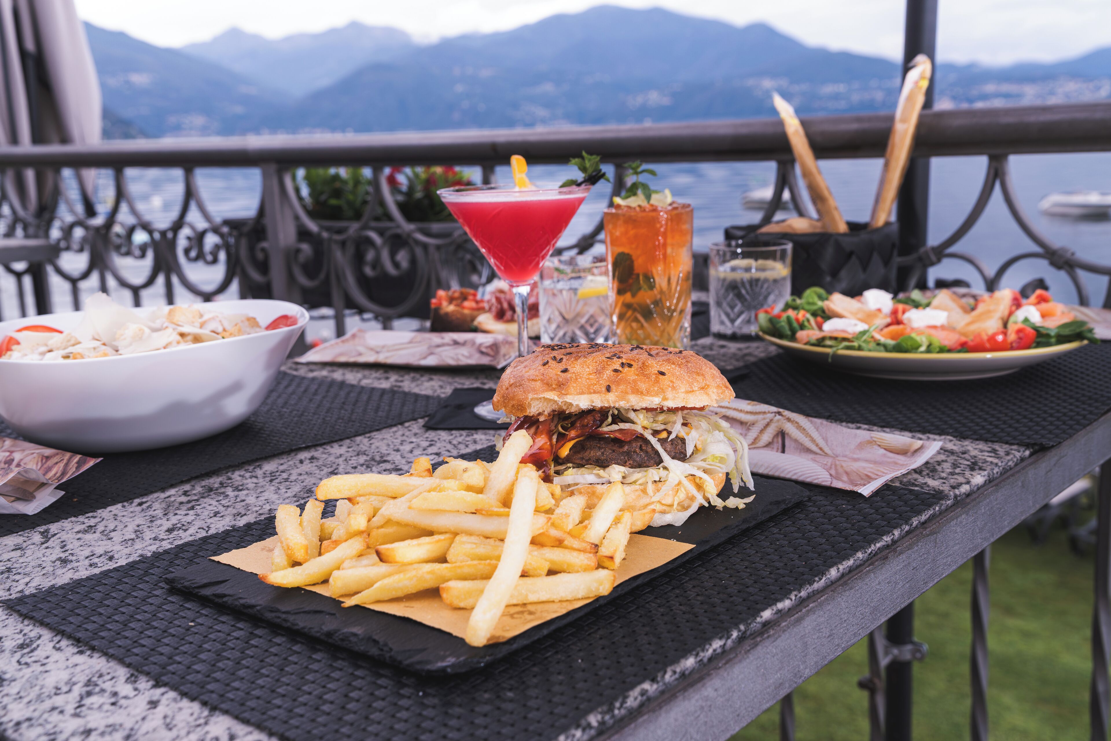 Una comida con hamburguesa, papas fritas, ensalada y bebidas sobre una mesa con vistas panorámicas.