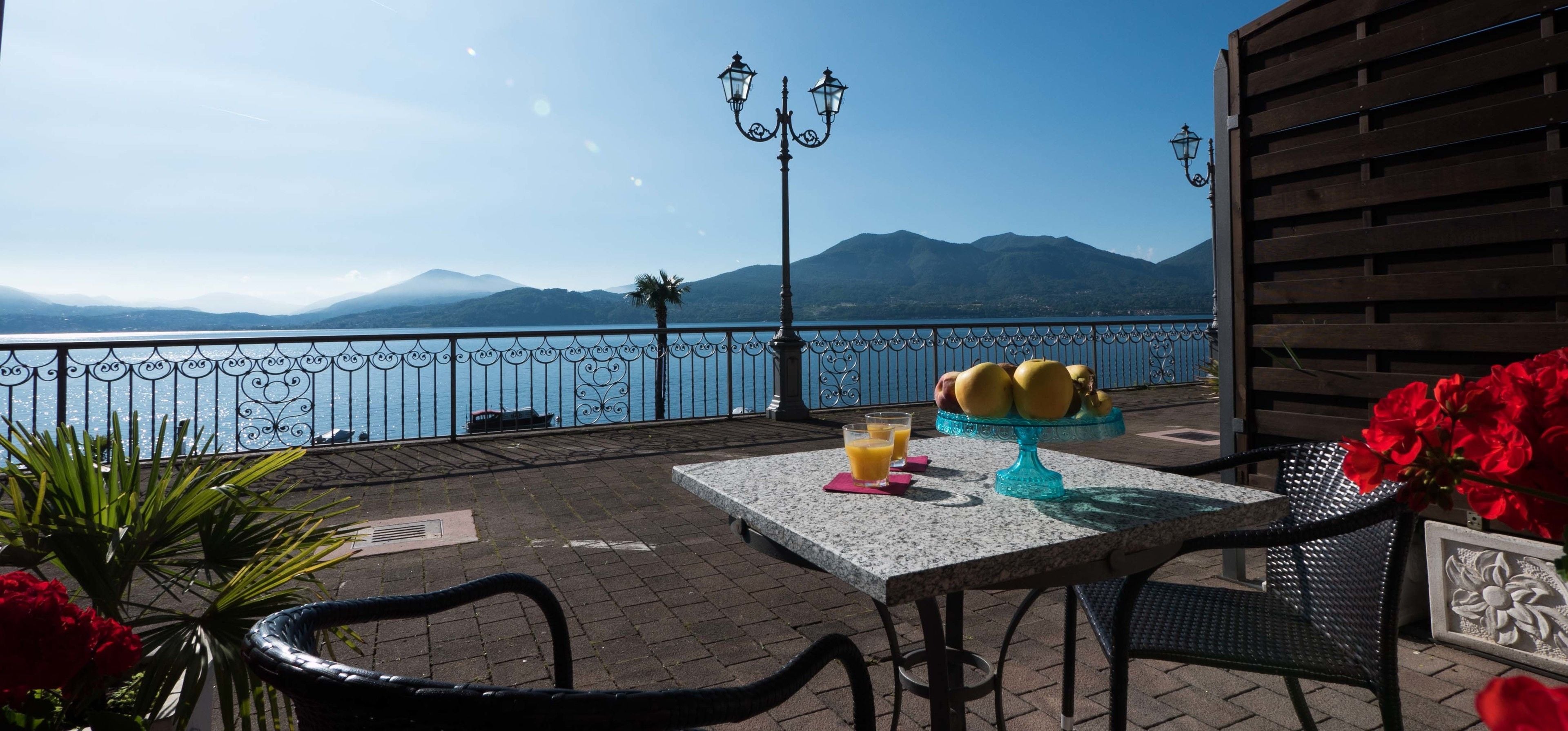A terrace with a table, chairs, a fruit display, and a view of the sea and mountains.