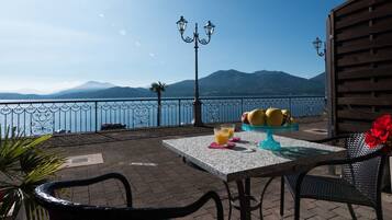 A terrace with a table, chairs, a fruit display, and a view of the sea and mountains.