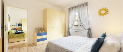 A bedroom with a bed, a wardrobe, a bedside table, and a window with curtains.
