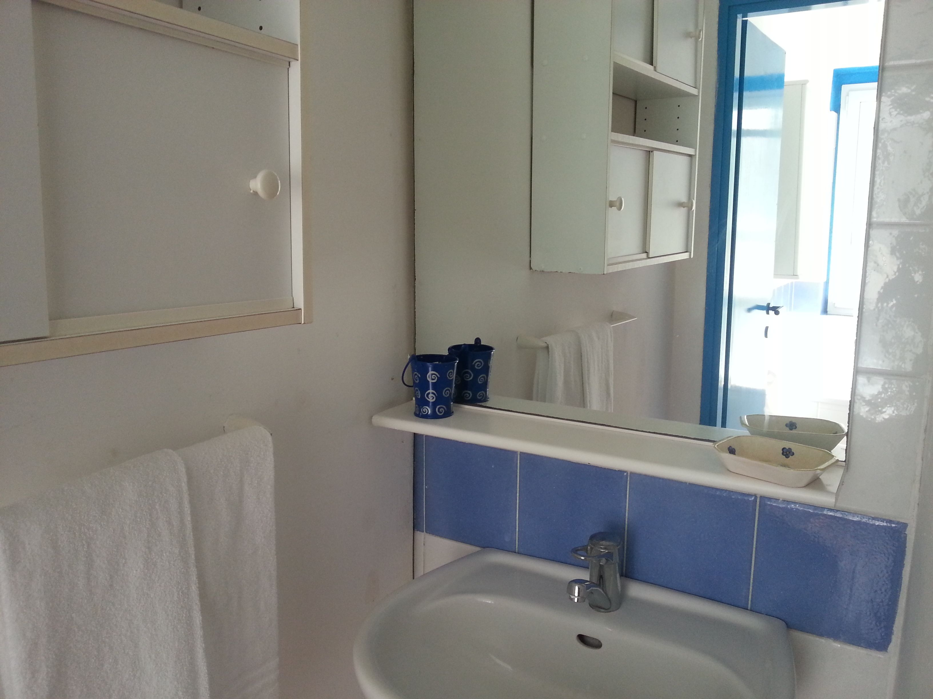 A bathroom with a white sink, blue-tiled walls, a mirror, and a towel rack.