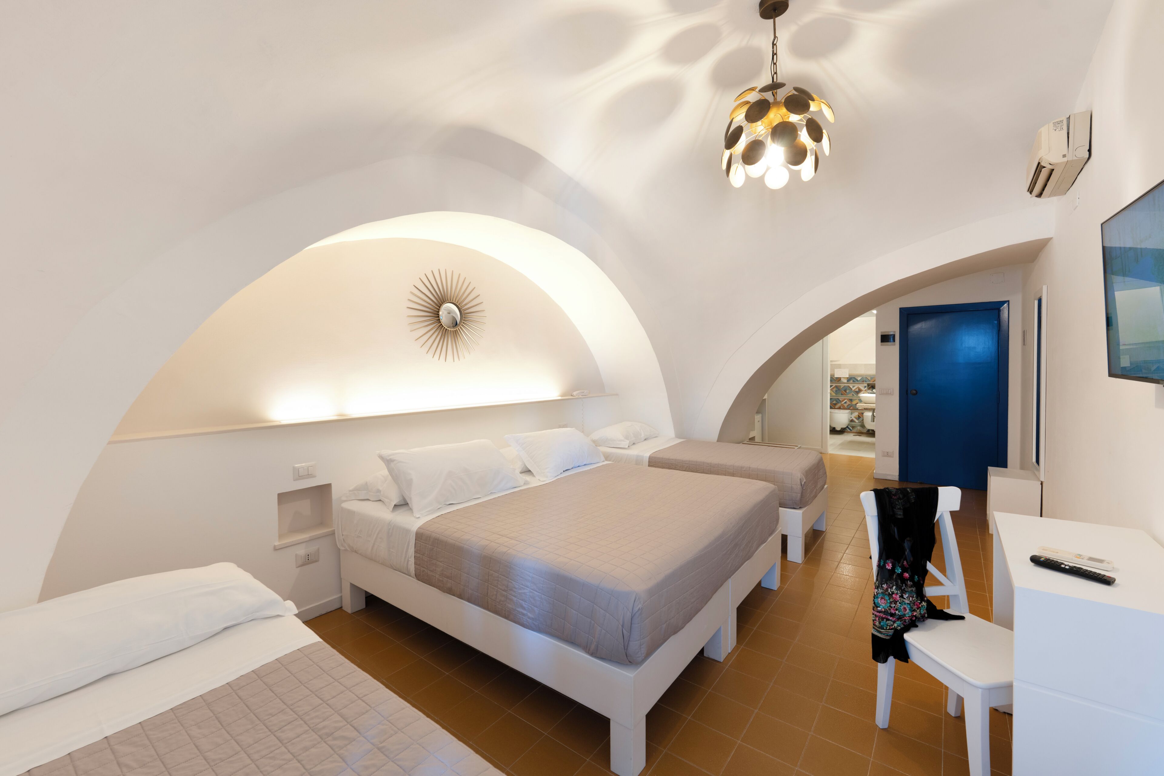 Ein Schlafzimmer mit einem großen Bett, einem Schreibtisch und einem Stuhl. Eine Tür und eine Deckenleuchte sind vorhanden.