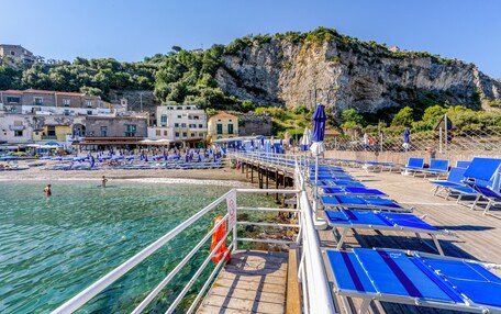 A coastal area with a pier, clear waters, and a rocky cliff.