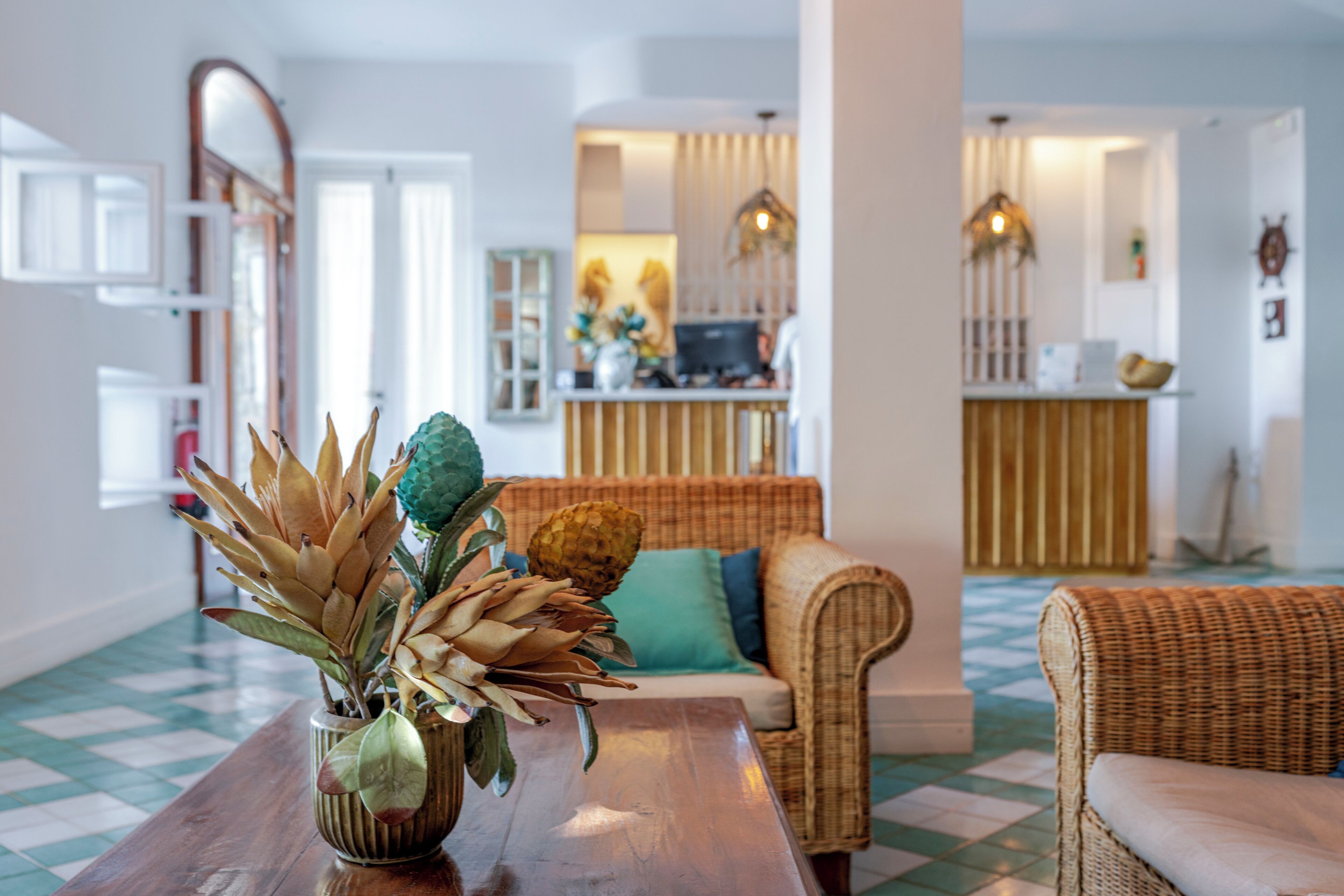 A living room with a wooden coffee table, a sofa, and a wicker chair. There is a decorative plant on the table.