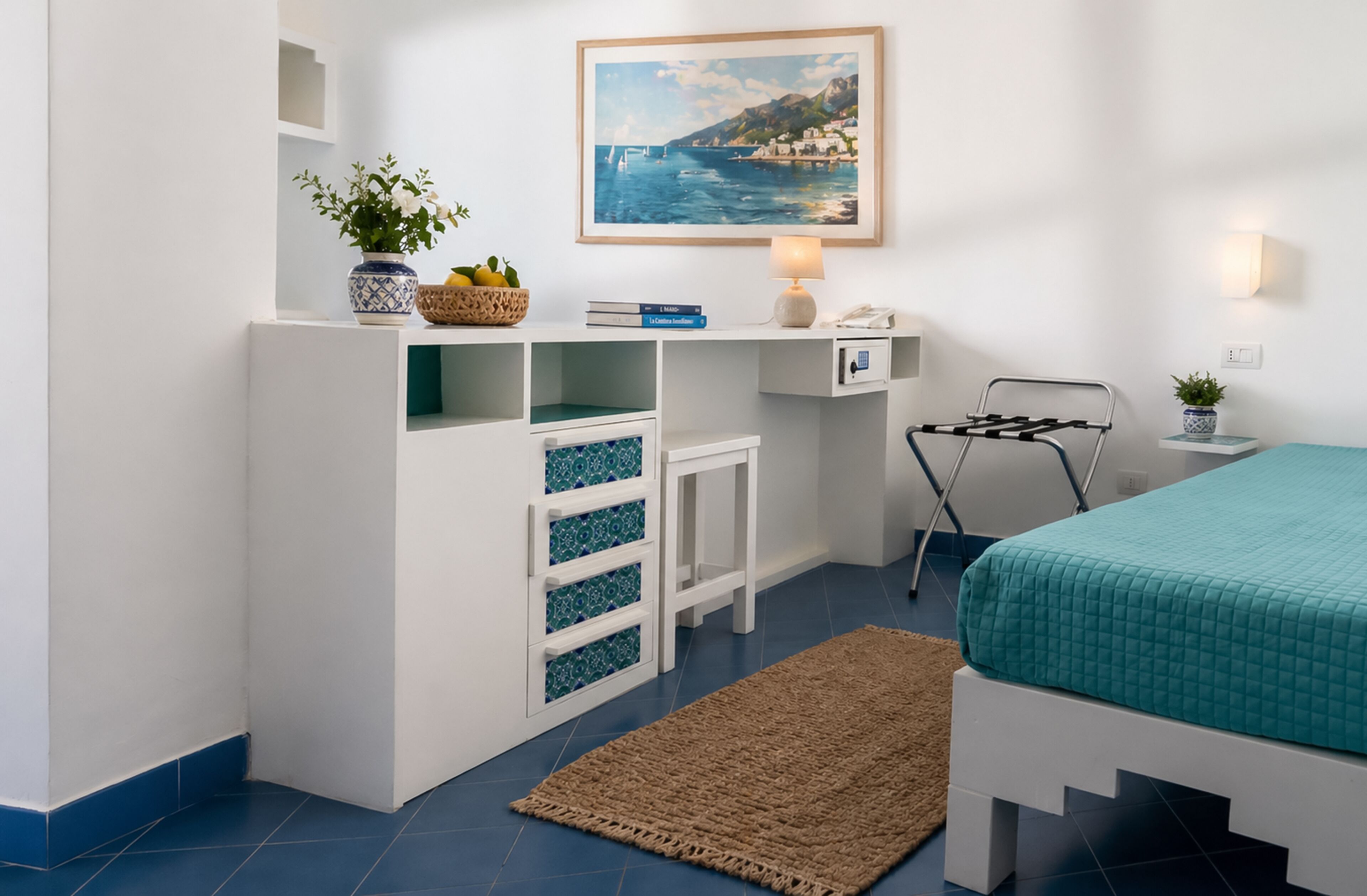 A bedroom with a bed, a desk with a lamp, a chair, a small table with a plant, and a painting on the wall.