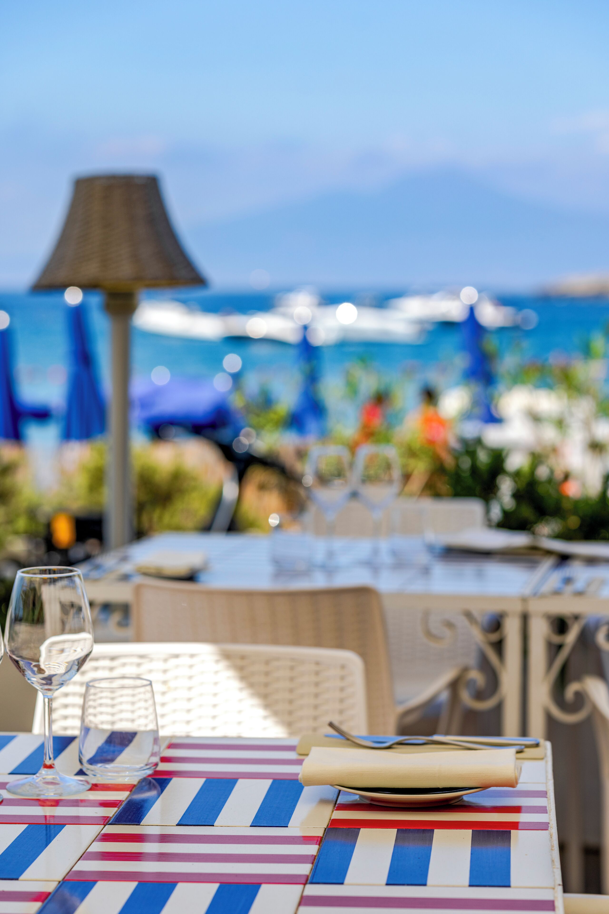 Un espace extérieur aménagé pour les repas, avec vue sur la mer, comprenant des tables, des chaises et une lampe.